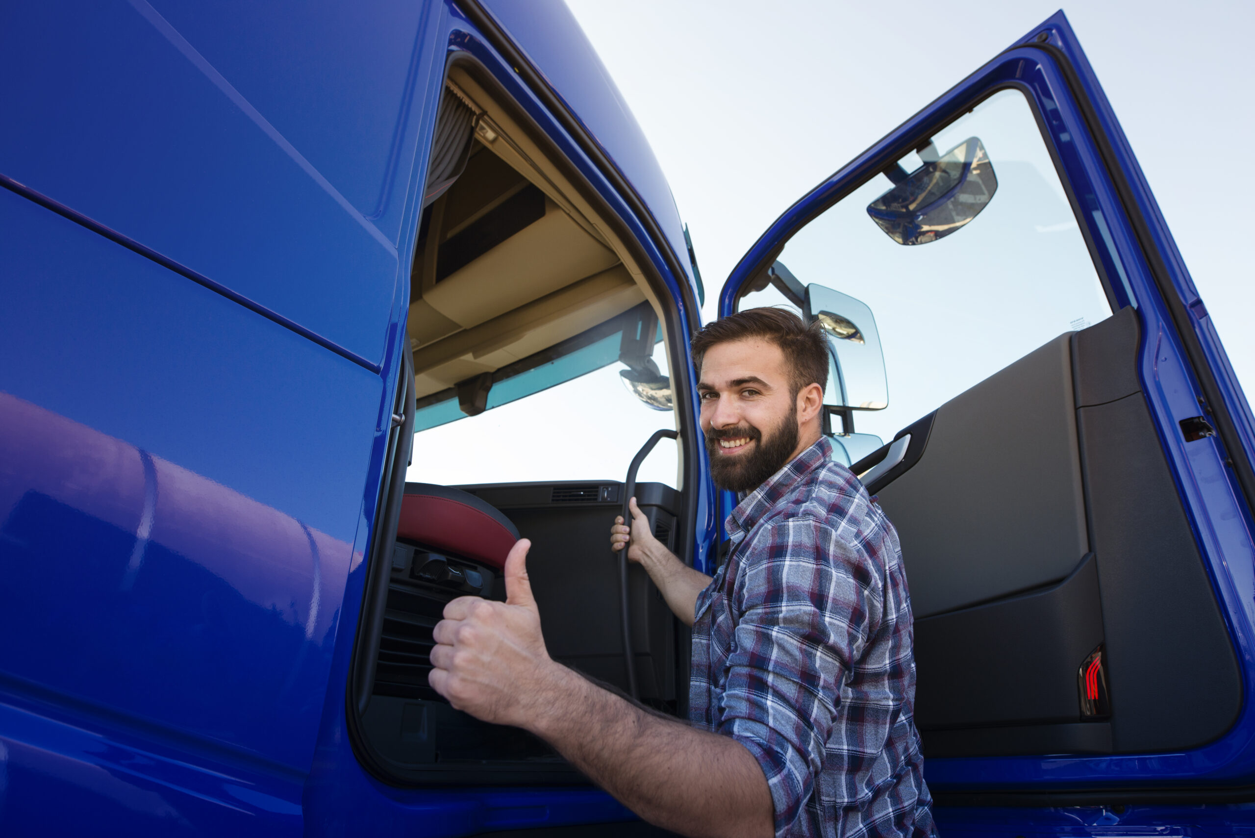 professional truck driver entering his truck long vehicle and holding thumbs up.